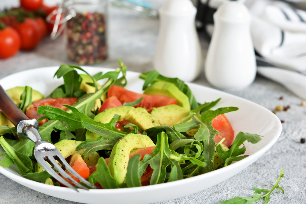 Salad with rucolla, tomatoes, avocado and sauce on the kitchen table. The view is close.